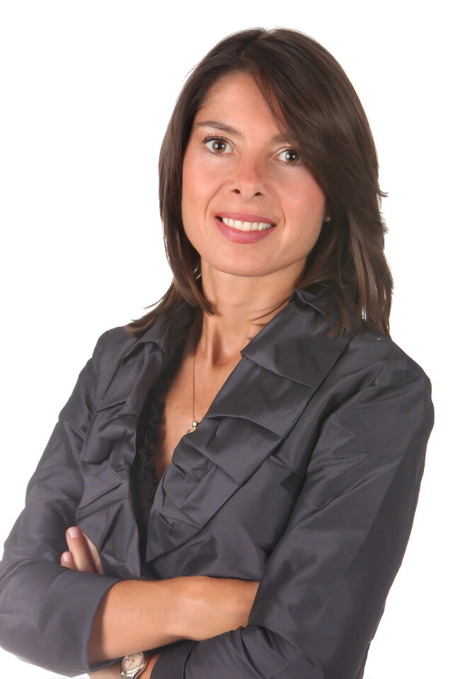 Retrato de Veronica Pepe, Principal de Valmore Management & Staffing, con traje gris carbón y blusa color crema en una oficina ejecutiva con paneles de nogal y luz natural cálida.