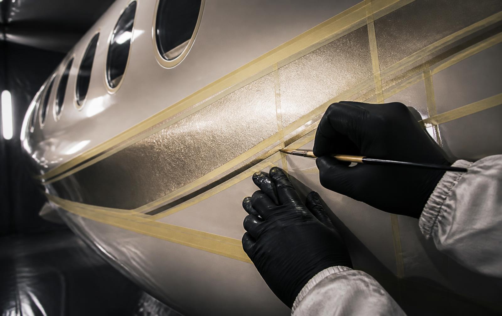 Technician hand-painting a pearlescent champagne livery stripe on a jet fuselage